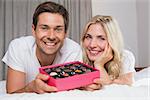 Portrait of a relaxed happy young couple with candies resting in bed at home