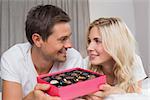 Relaxed happy young couple with candies resting in bed at home