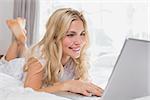 Happy casual young woman using laptop in bed at home