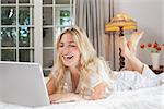 Cheerful casual young woman using laptop in bed at home