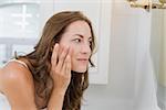 Side view of a beautiful young woman examining her face in the bathroom at home