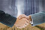 Composite image of business handshake against cityscape projection over yellow fields