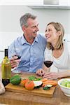 Cheerful couple with wine glasses in the kitchen at home