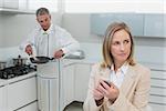 Businesswoman text messaging while man preparing food in the kitchen at home