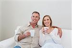Relaxed loving couple with coffee cups looking away in living room at home