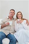 Relaxed loving couple with coffee cups looking away in living room at home