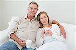 Relaxed loving couple with coffee cups in living room at home