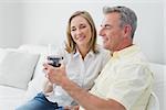 Happy relaxed couple with wine glasses sitting on sofa at home