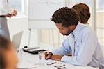 Side view of a young businessman writing notes in meeting at the office