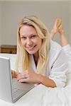 Full length of woman using laptop while lying in bed at home