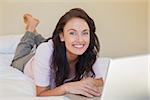 Portrait of happy woman with laptop lying in bed at home