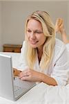 Blond woman using laptop while lying in bed at home