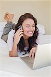 Happy woman on call while using laptop in bed at home