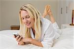 Blond woman reading text message on mobile phone while lying in bed at home