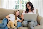 Smiling woman using laptop by daughter on sofa at home