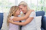 Happy mother and daughter rubbing noses while sitting on sofa at home