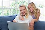 Smiling mother and daughter using laptop together on sofa