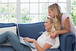 Side view of happy mother and daughter using laptop in living room