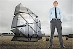 Happy businessman standing with hands in pockets against landscape with bales of straw