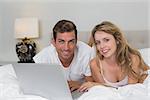 Portrait of a smiling young couple using laptop in bed at home