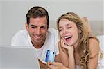 Happy young couple doing online shopping through laptop and credit card at home