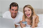 Happy young couple doing online shopping through laptop and credit card at home