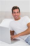 Portrait of a smiling young man using laptop in bed at home