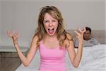 Angry young woman shouting with man in background in bed at home