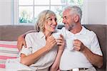 Smiling relaxed mature couple with coffee cups in the living room at home