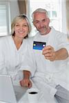 Portrait of a happy mature couple holding out credit card at home