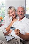 Happy mature couple doing online shopping through laptop and credit card at home