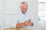 Smiling relaxed mature man text messaging at home