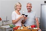 Happy mature couple toasting wine glasses while preparing food in the kitchen at home