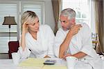 Serious mature couple sitting with home bills and calculator at table