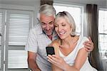 Cheerful mature couple reading text message at home