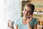 Smiling young woman drinking coffee while using mobile phone in the coffee shop