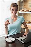 Smiling young woman with coffee cup using laptop at counter in the coffee shop