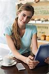 Smiling young woman with coffee cup using digital tablet at counter in the coffee shop