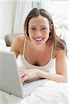 Smiling relaxed young woman using laptop in bed at home