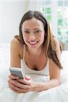 Close-up of a smiling young woman text messaging in bed at home