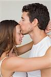 Side view of a loving young man kissing woman on forehead at home
