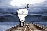 Fish jumping out of light bulb bowl against train tracks leading to misty mountains