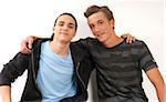 Portrait of two young men, friends with arms around shoulders, looking at camera and smiling, studio shot on white background