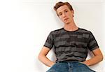 Portrait of young man sitting and leaning against wall, looking at camera, studio shot on whire background