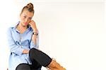 Portrait of young, blond woman sitting and leaning against wall, looking at camera, studio shot on white background