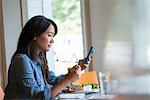 A woman eating a salad, and checking her phone.