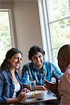 Three people seated at a cafe table talking.