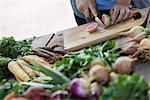 A person chopping freshly picked vegetables and fruits.