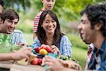 A summer party outdoors. Adults and children around a table.