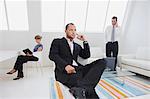 Three business people in an office, one on the phone, one working on a digital table, and one seated in a chair.